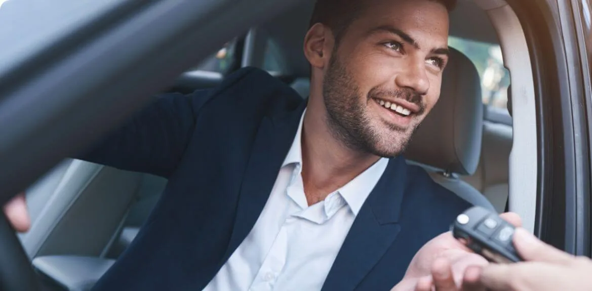 Lächelnder Mann bekommt Autoschlüssel für seinen Firmenwagen übergeben.